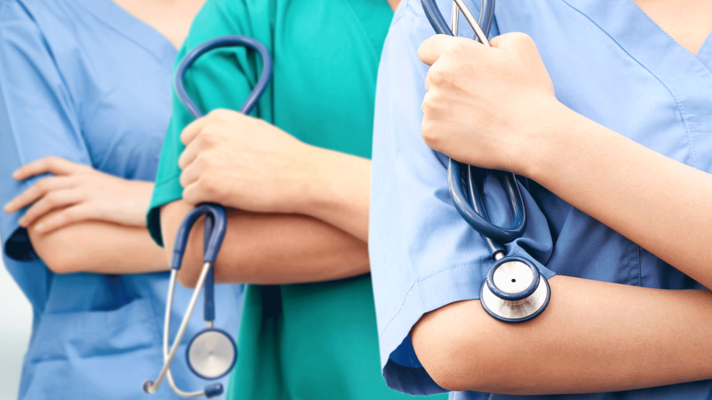 Three healthcare professionals in scrubs, each holding a stethoscope with crossed arms, are shown standing in a line.