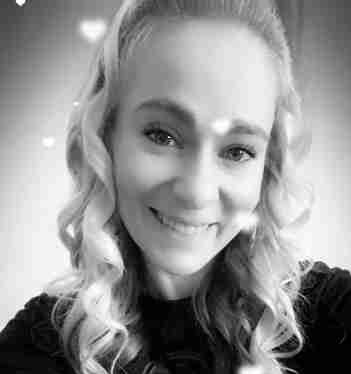 A black and white photo of a person with long, curly hair, smiling at the camera. Heart-shaped effects are overlaid on the image, capturing a moment of joy in their thriving career.