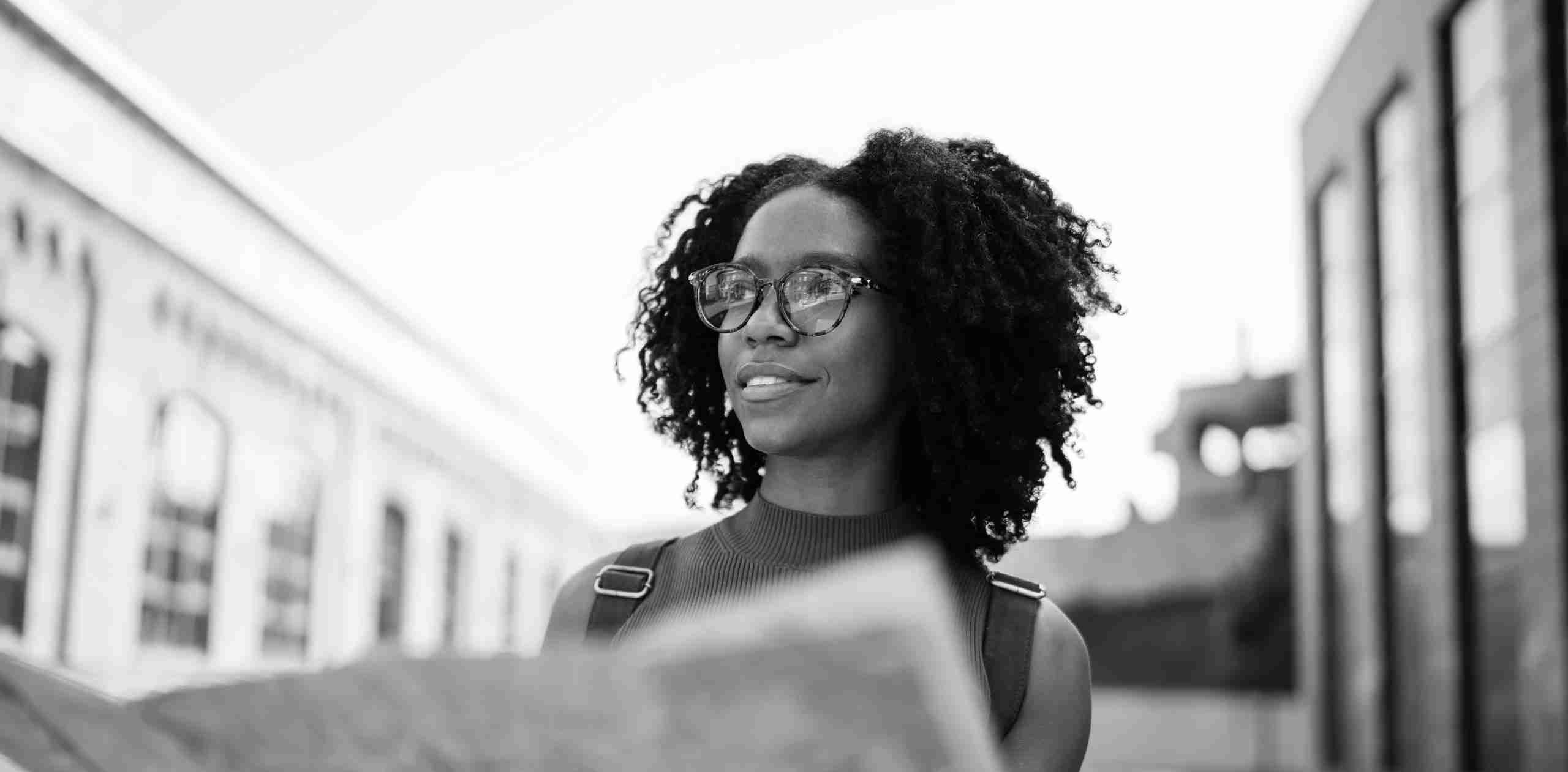 A person with glasses holds and reads a map while standing on an empty street.