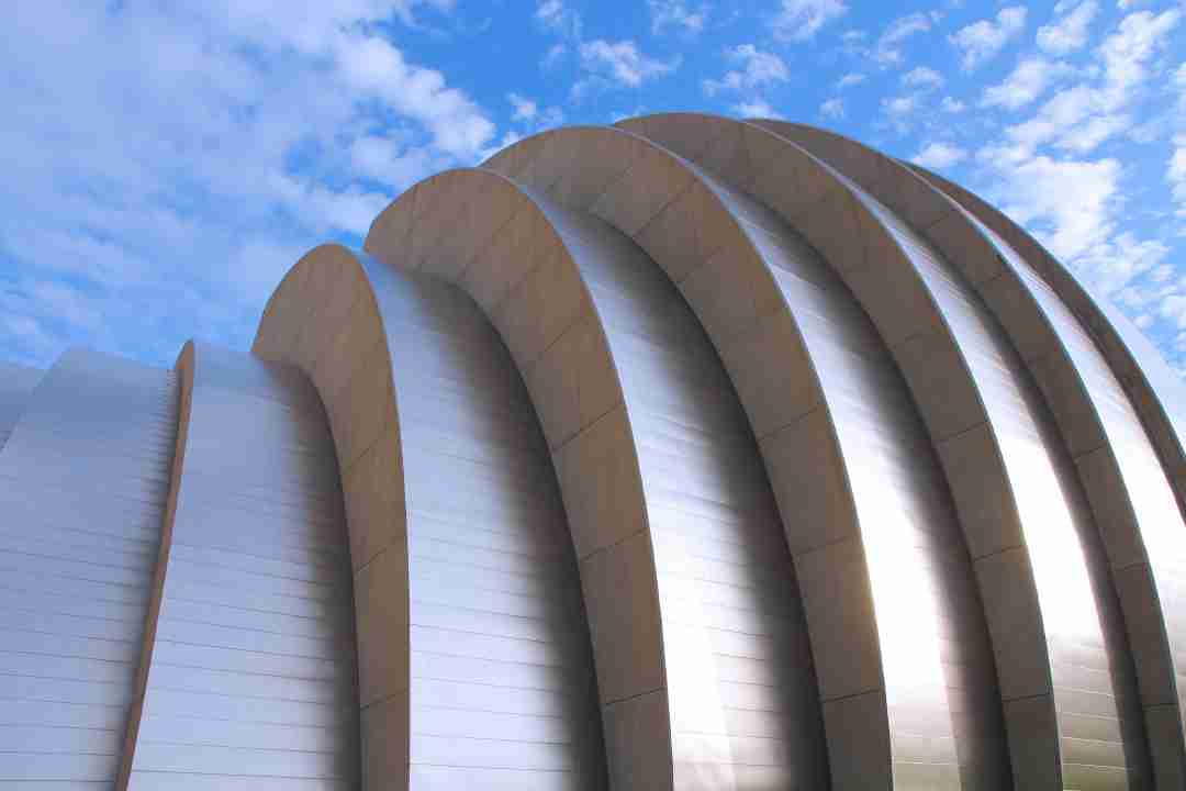 Curved, metallic, ribbed structure with overlapping arches set against a blue sky with scattered clouds—an inspiring sight reminiscent of the innovative designs supported by a Kauffman grant.
