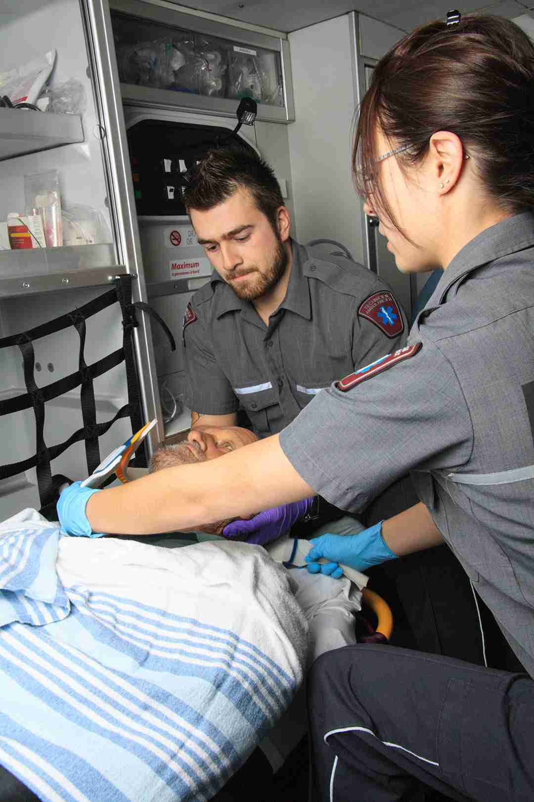 Two paramedics attend to a patient on a stretcher inside an ambulance, providing medical care with focused attention.