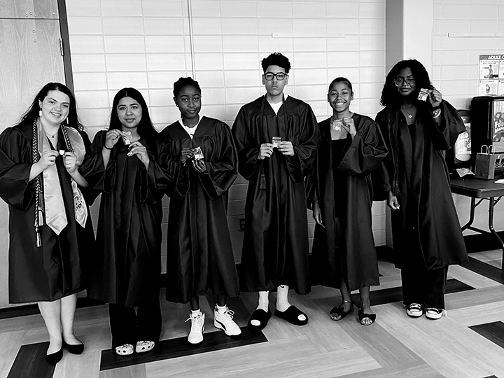 Six students in graduation gowns stand indoors, holding medals and smiling for the camera—a proud moment featured in the Kansas City education impact newsletter.