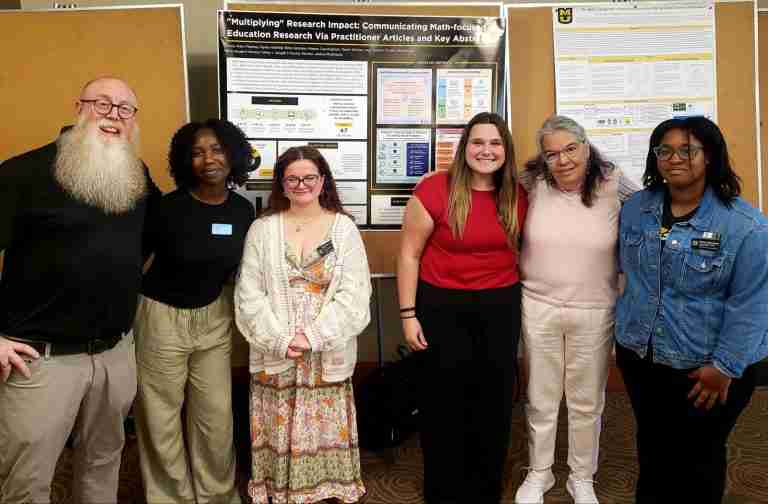 Six people stand in front of research posters on display boards, posing for a group photo at an academic event that inspires you to not abandon your dreams—achieve them.