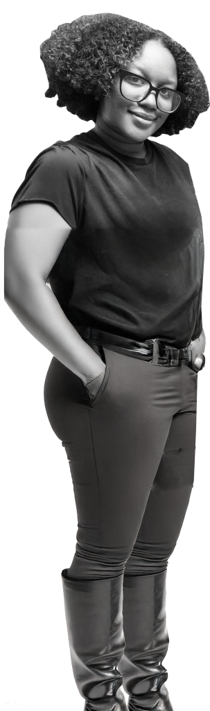 A person with curly hair, glasses, a black t-shirt, fitted pants, and knee-high boots stands with hands in pockets, facing slightly to the side—ready to deliver the annual report.
