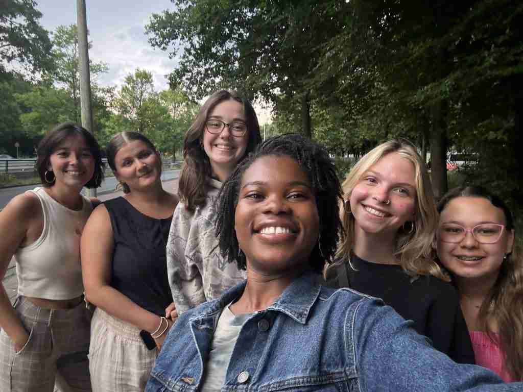 Six young women, including a study abroad psychology student, stand outdoors smiling for a group selfie with trees in the background.