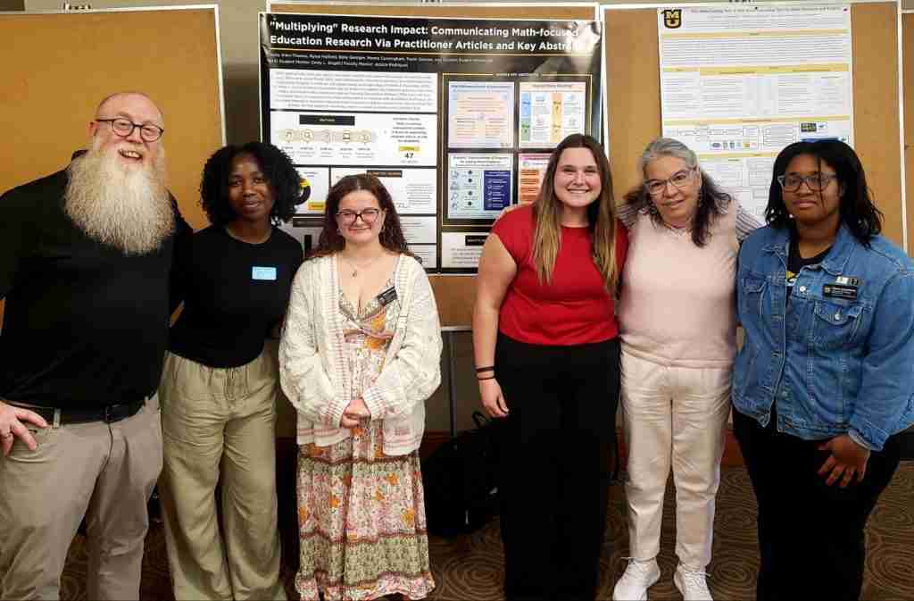 Six people stand in front of research posters displayed on bulletin boards, posing for a group photo in an indoor setting that highlights their dedication to resilience and recovery.