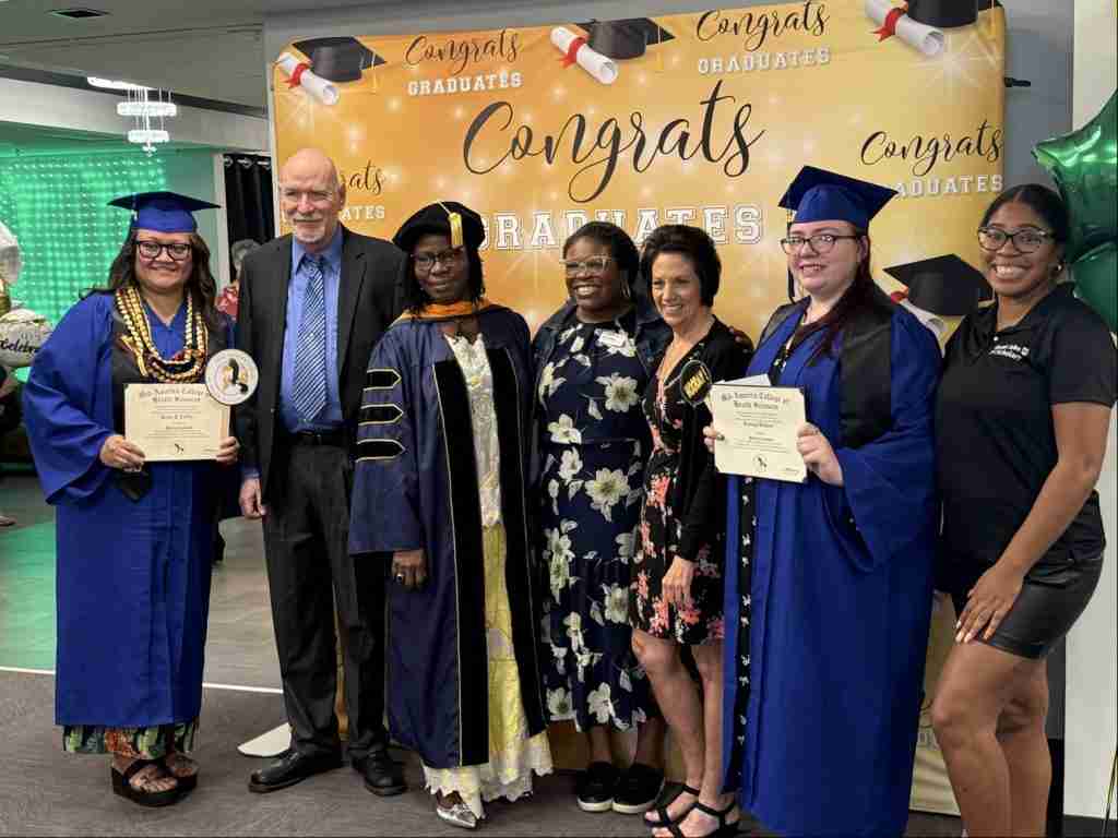 A group of people, including graduates in blue caps and gowns, pose with certificates in front of a "Congrats Graduates" banner, ready to launch your future at this inspiring graduation event.