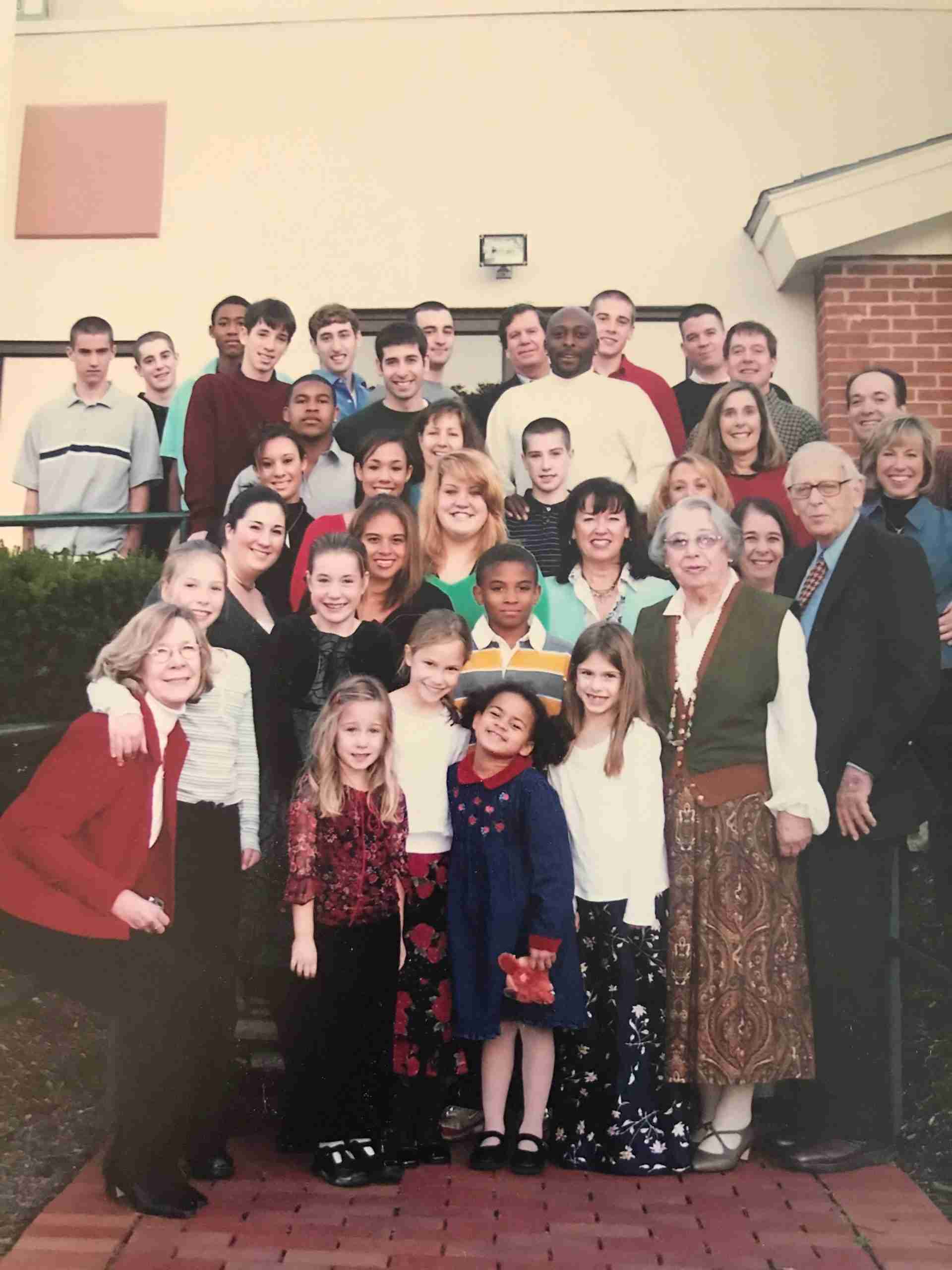 A large multigenerational group of people pose together outdoors on steps in front of a building, smiling at the camera.