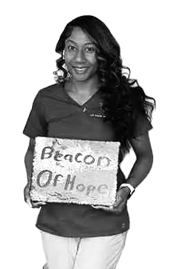 A woman standing and smiling, holding a sign that says “Beacon Of Hope,” perfect for inclusion in a press kit.