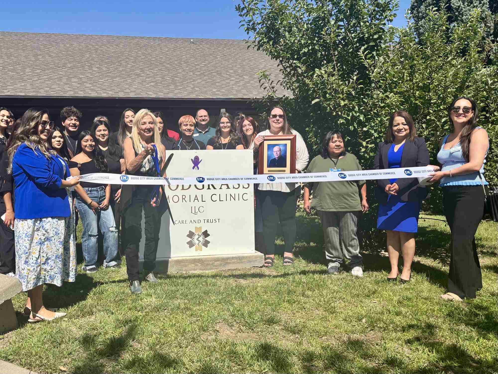A group of people stand outside a building for a ribbon-cutting ceremony in front of a sign that reads “Sorakusa Memorial Clinic LLC,” celebrating Ten Years of Impact and honoring Ten Years of Scholars.