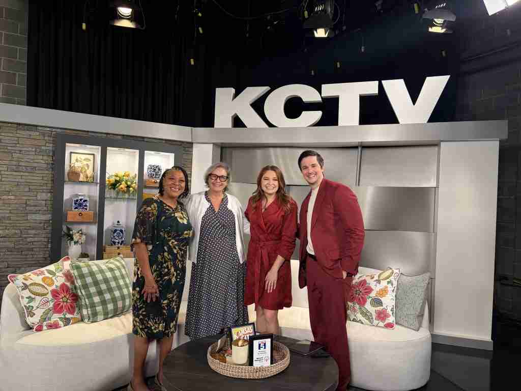 Four people stand and smile together on a TV studio set with “KCTV” displayed in large letters behind them. The set, featuring a couch, chairs, and decorative pillows, creates a welcoming backdrop as the group discusses back to school tips and opportunities for college scholarships and skills training.